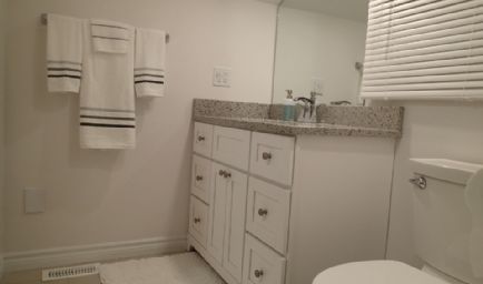 Bathroom with white vanity, toilet, towels, and a window with blinds.