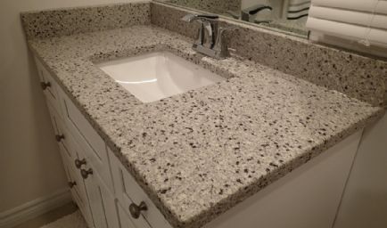Bathroom vanity with white cabinets, speckled light granite countertop, and a white sink.