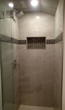 Shower stall with light gray tiles, dark mosaic accent, glass door, and recessed shelf.
