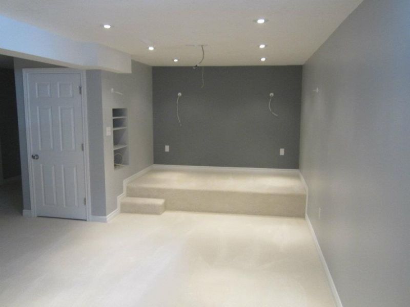 Empty gray-walled room with a raised platform and built-in shelving. White door and off-white carpet.