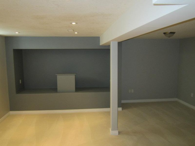 A gray-painted basement room with a recessed alcove, carpeted floor, and white support beam.