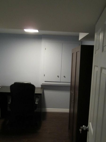 Home office with desk, chair, cabinets, and dark wood flooring. Light blue walls, dark wood closet, and white door.