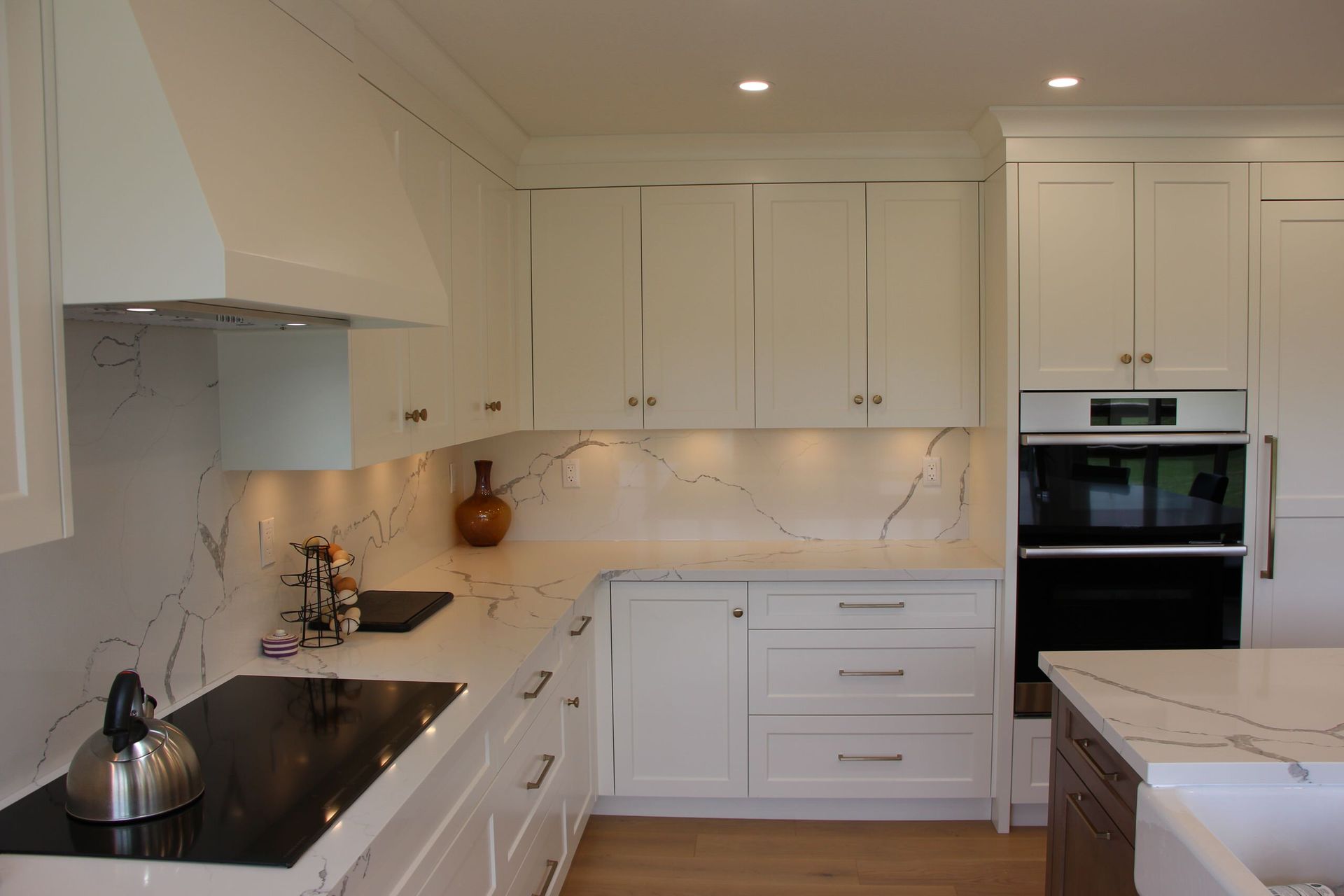 White modern kitchen with marble countertops, white cabinets, and stainless steel appliances.