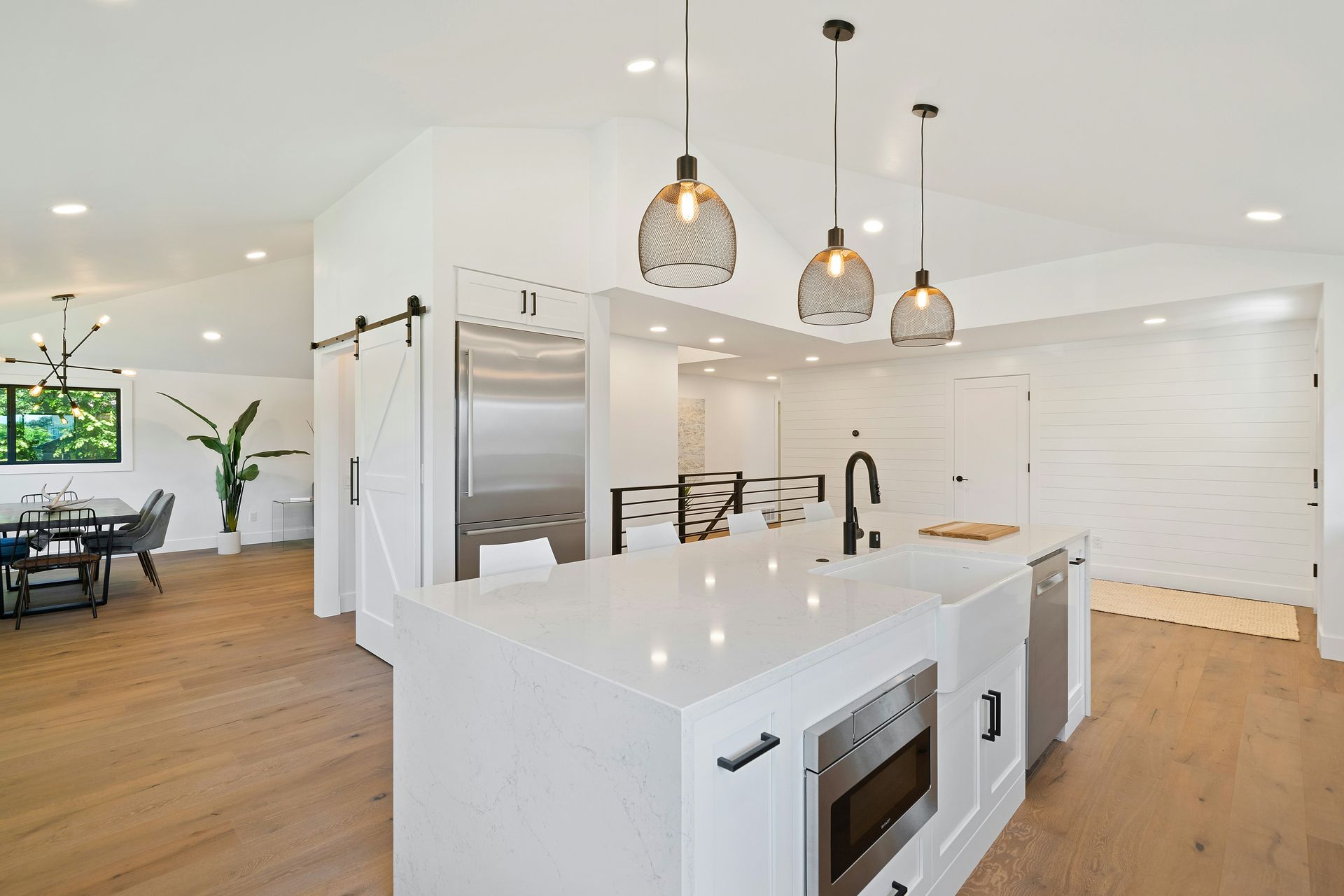 Modern white kitchen with island, stainless steel appliances, and wooden floors.