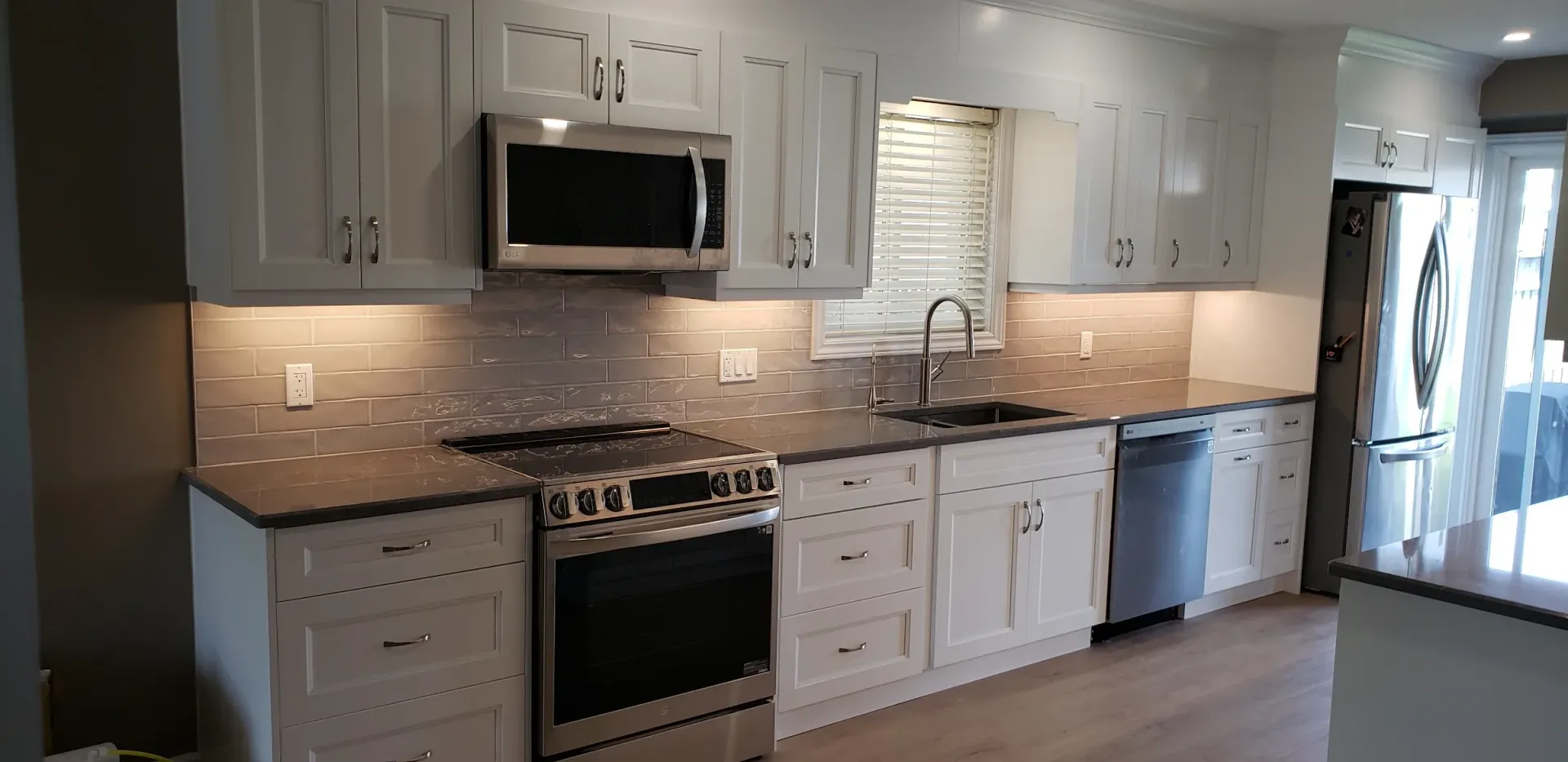 Bright white kitchen with stainless steel appliances, gray countertops, and white cabinets.