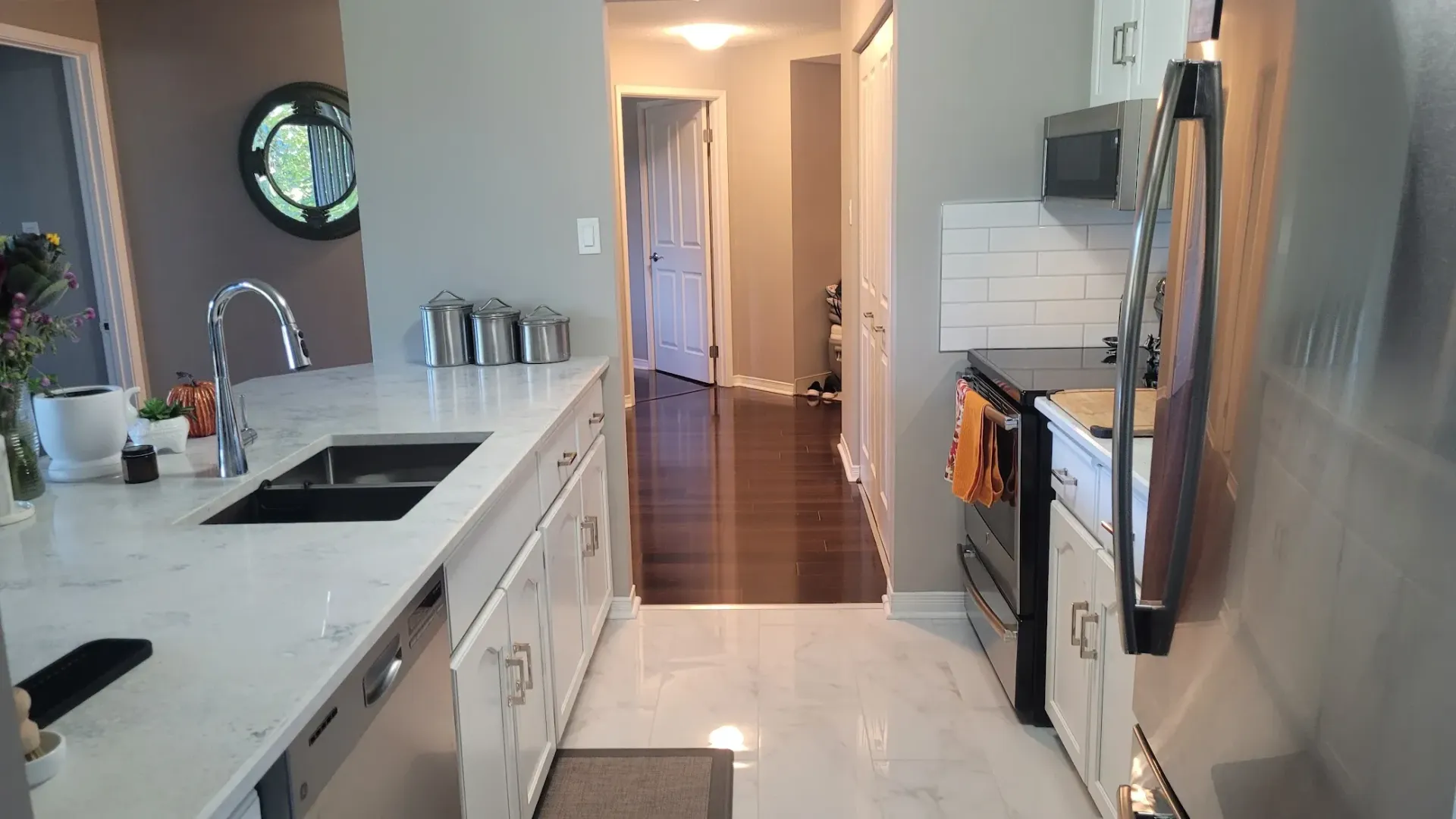 Kitchen with white countertops, dark sink, and wooden floor leading to a hallway.