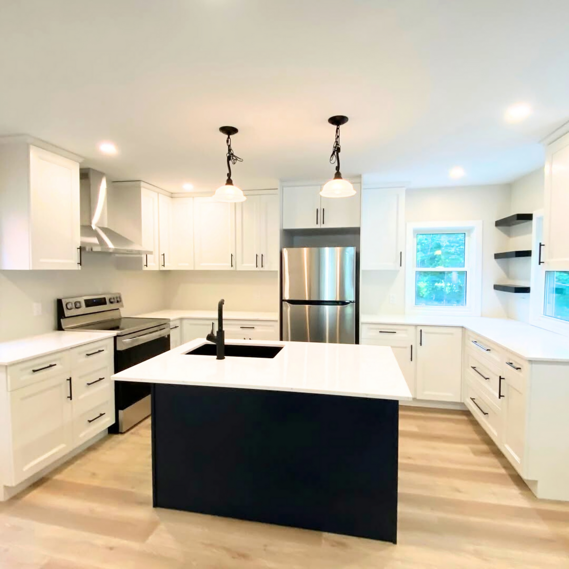 Modern kitchen with white cabinets, black island, stainless steel appliances, and light wood floors.