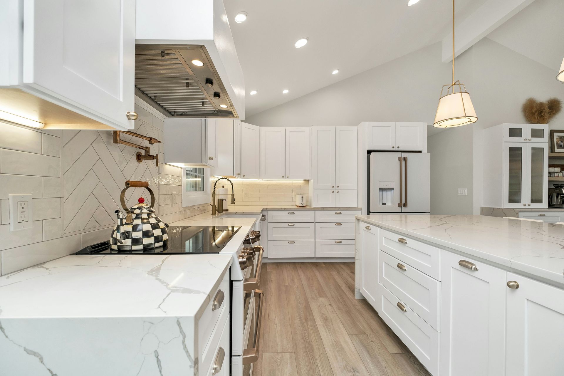 White kitchen with marble countertops, stainless steel appliances, and a central island.