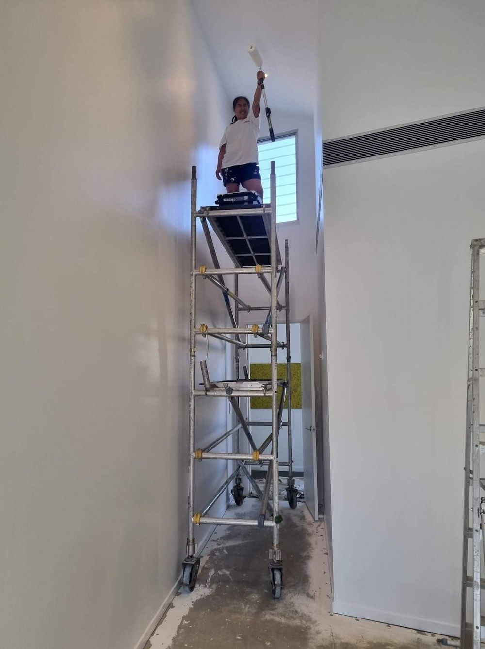 A Painter Is Standing On A Scaffolding Painting A Wall — Ross Painting In Ciccone, NT