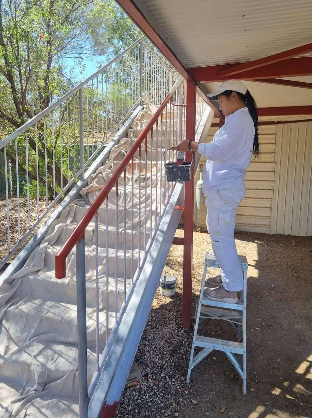 A Woman Is Standing On A Ladder Painting Stairs — Ross Painting In Ciccone, NT