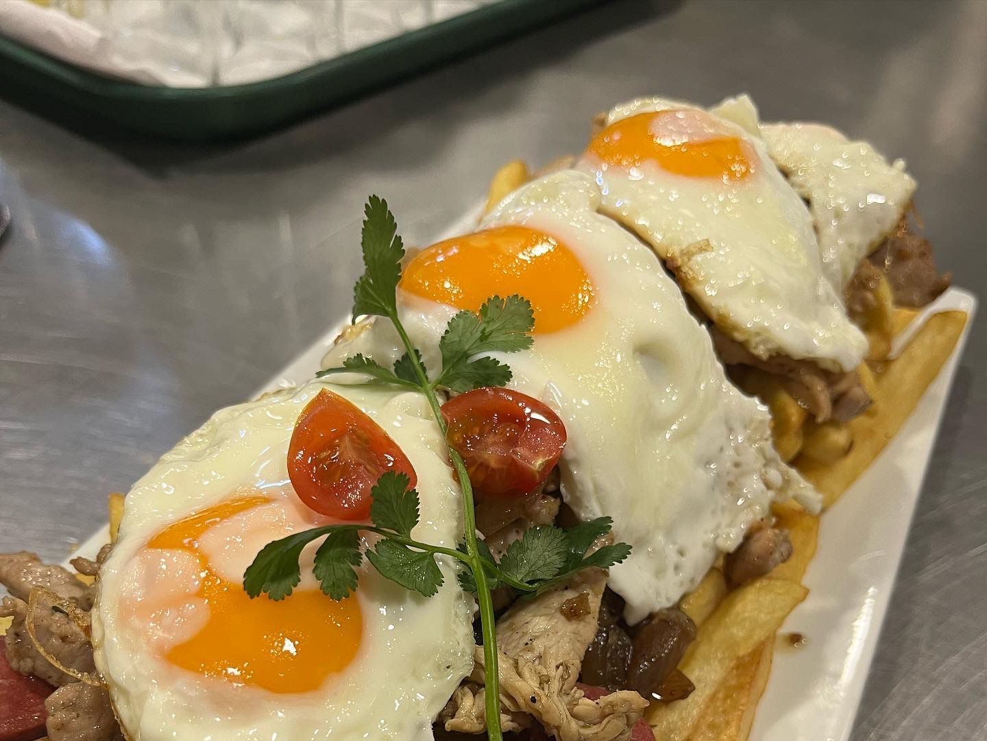 Huevos fritos sobre una baguette cargada con carne, patatas fritas y tomates; entorno de restaurante.