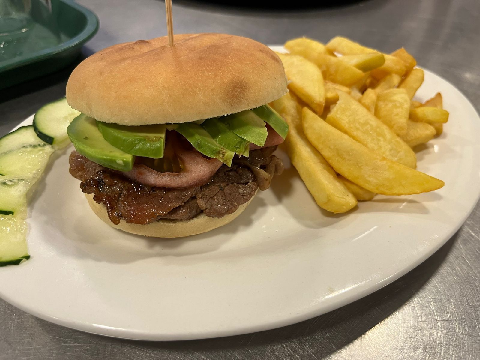 Hamburguesa con patatas fritas y rodajas de pepino en un plato blanco.