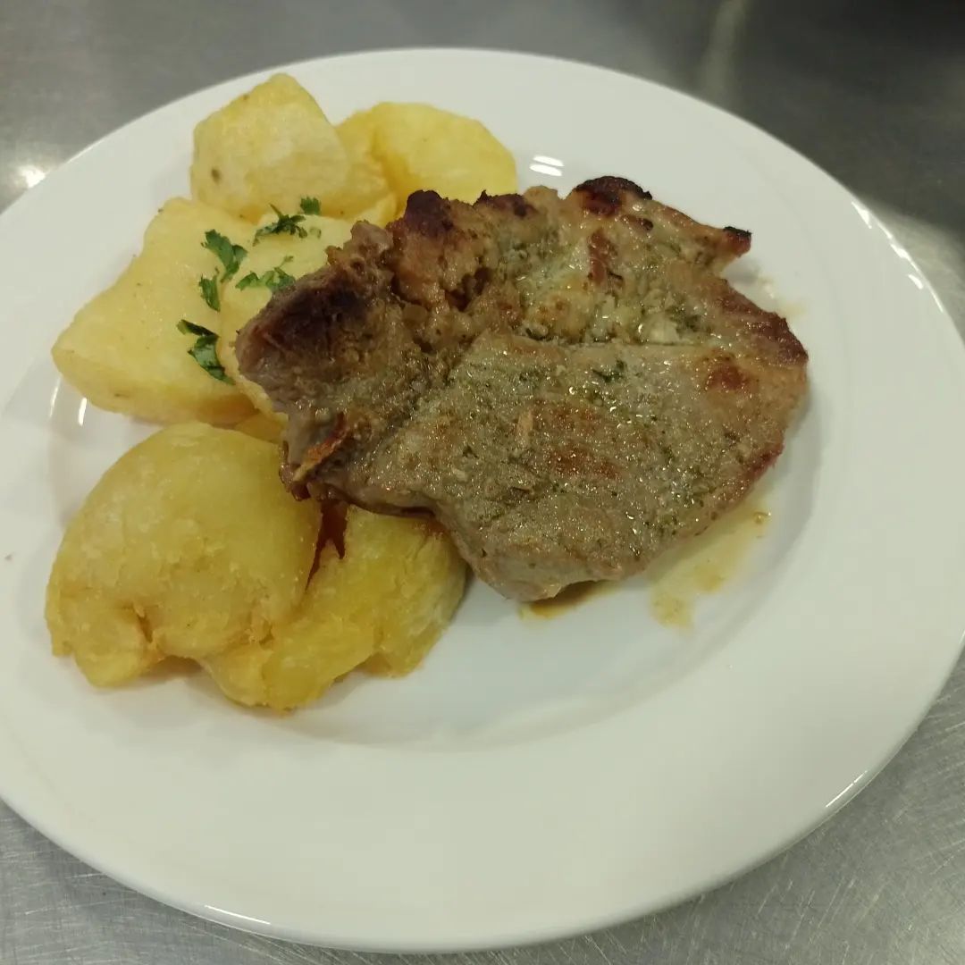 Chuleta de cerdo con patatas en un plato blanco.