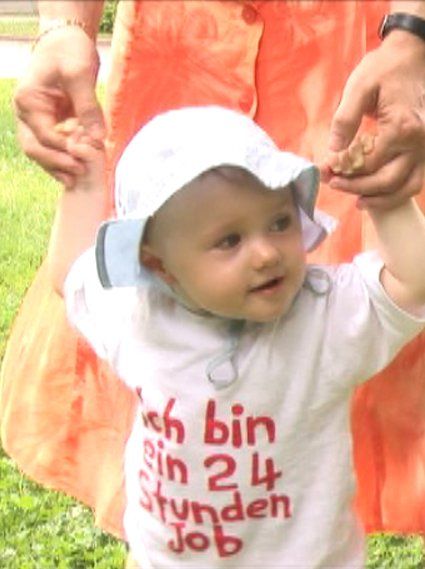 Ein 2-jähriges Mädchen geht an den Händen und schaut dabei neugierig nach links.