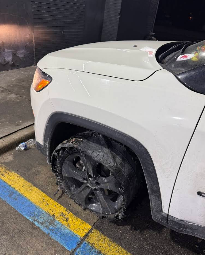 White Jeep with shredded front tire parked on a blue and yellow painted curb at night.