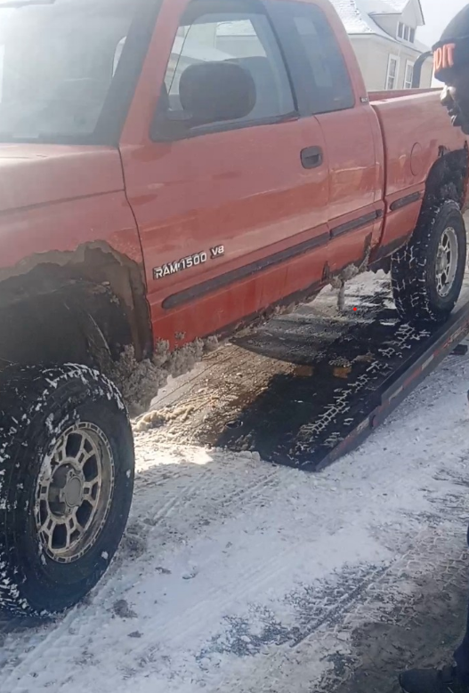 Red pickup truck on a snowy ramp, side view. Tire with snow, man watching.