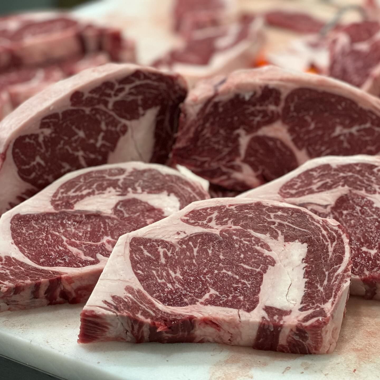 A bunch of raw steaks are sitting on a cutting board.