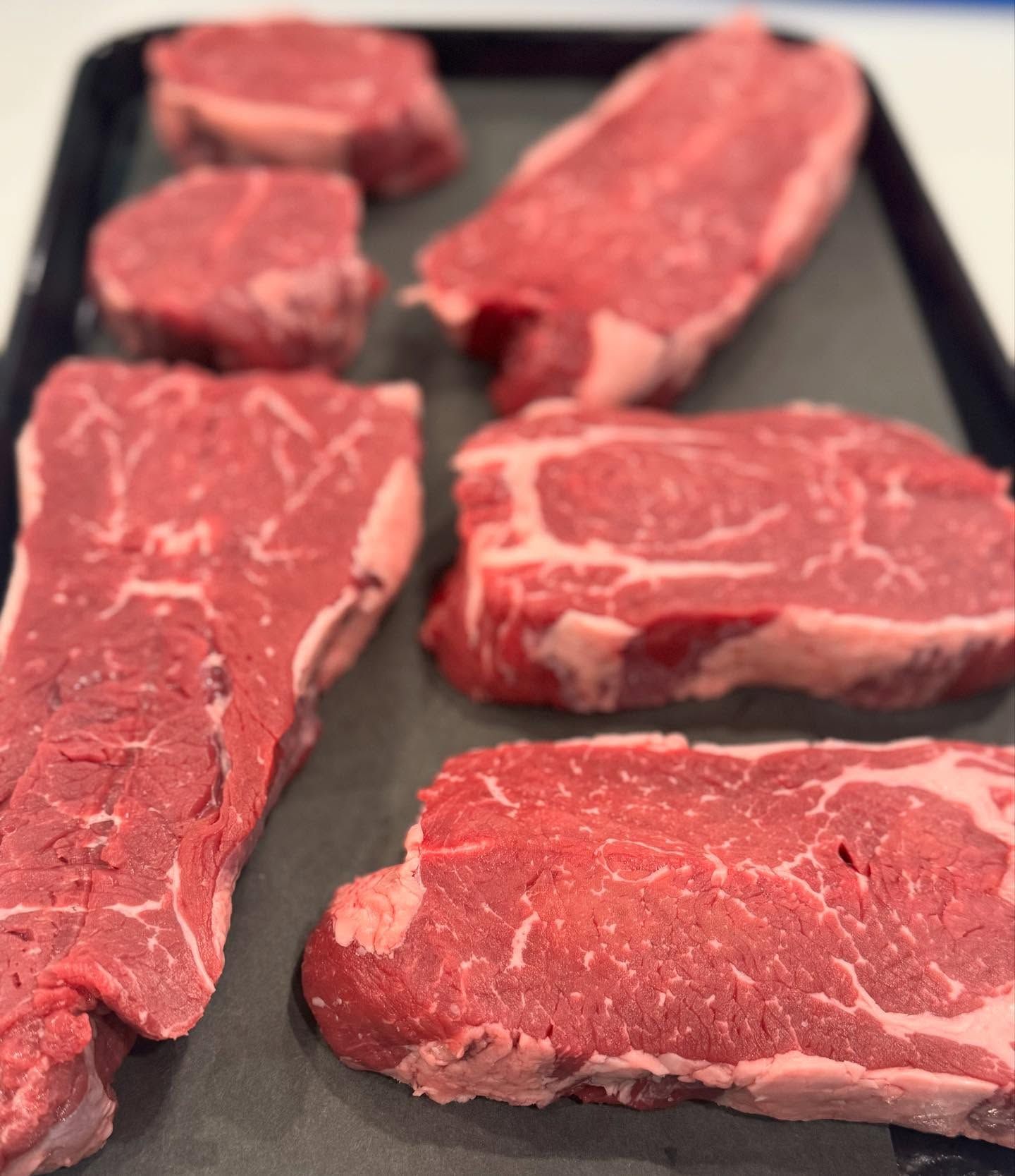 A tray of raw steaks is sitting on a table.