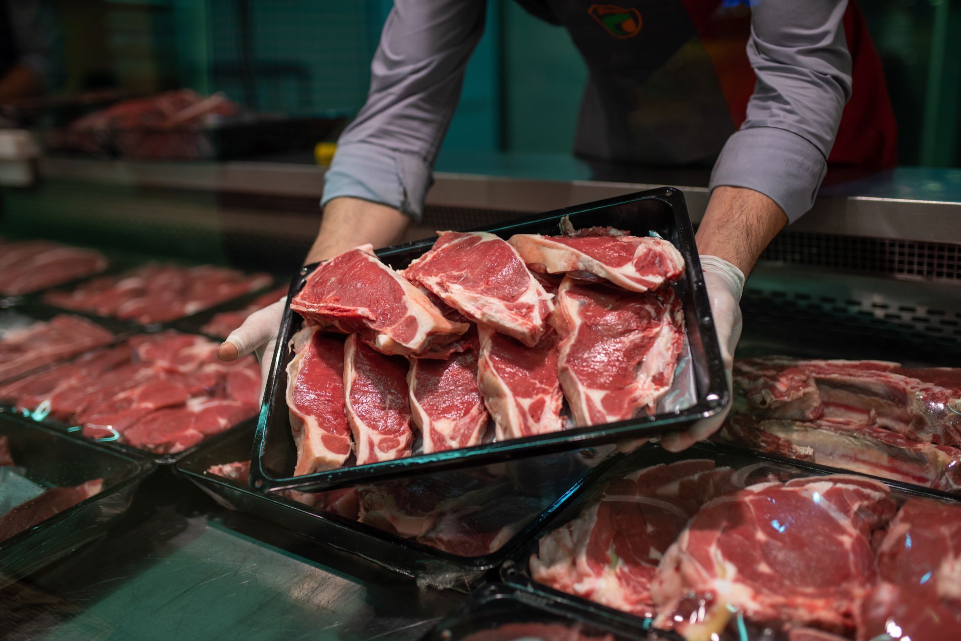 A person is holding a tray of meat in a butcher shop.