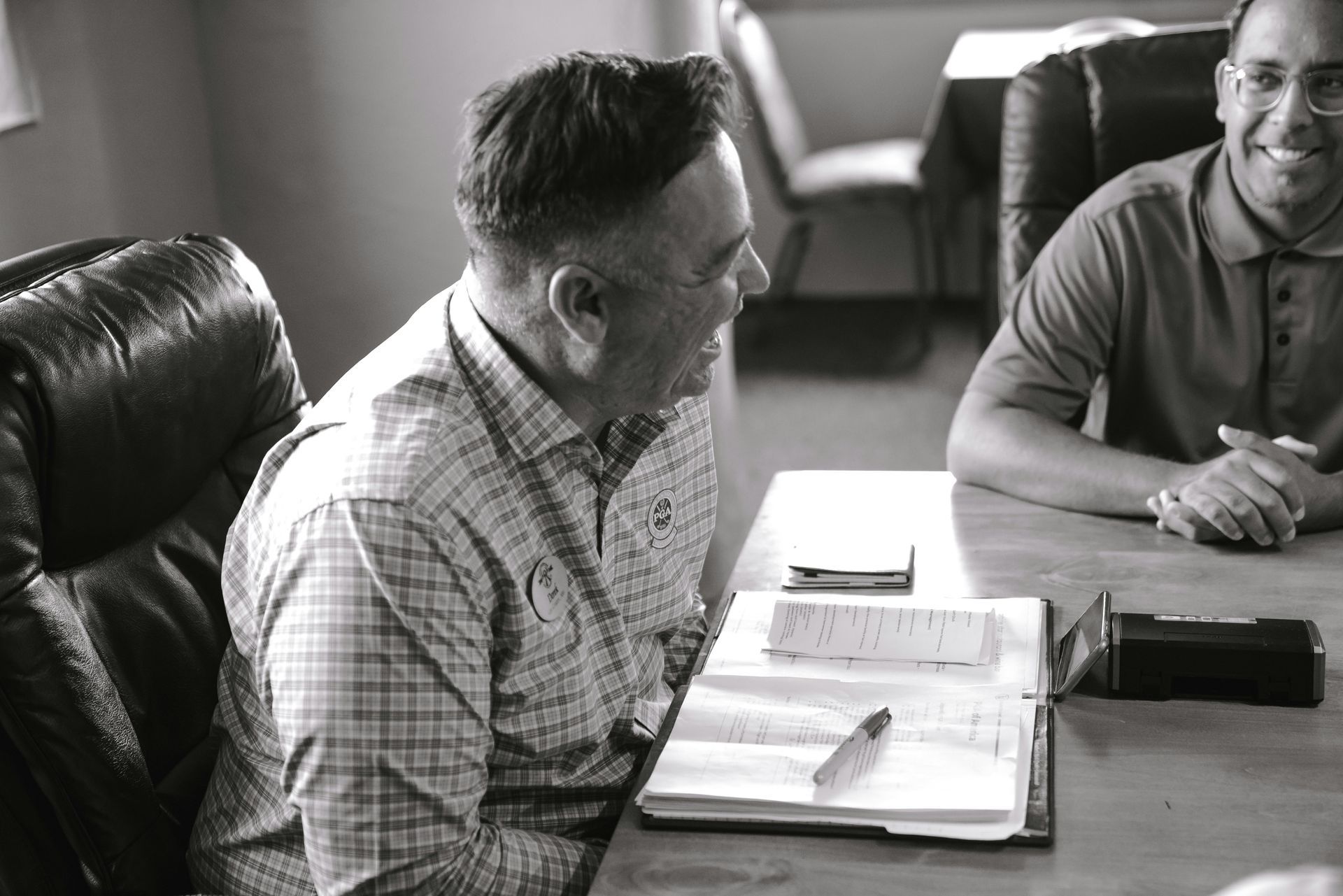 Two men are sitting at a table with a bible on it.