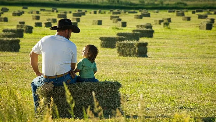 Man in cowboy hat sitting on bale of hay with young child