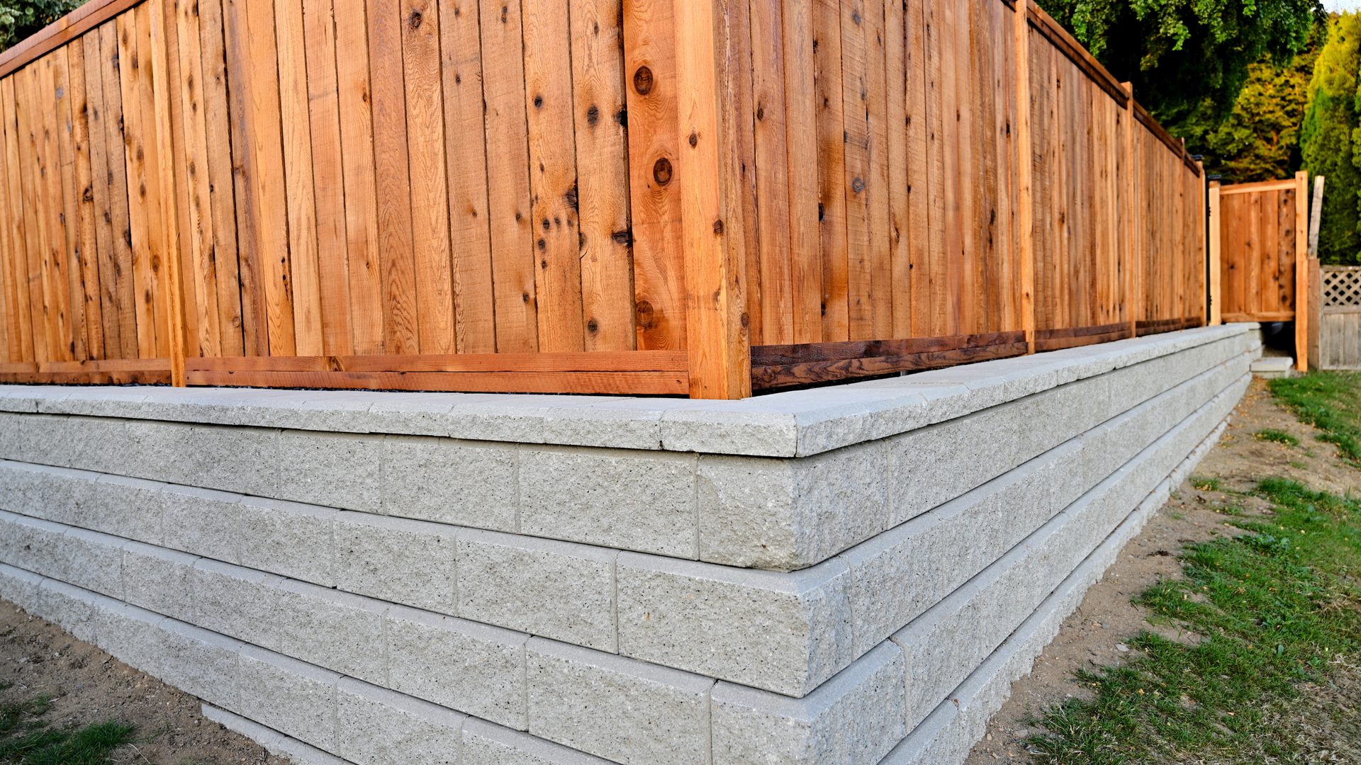 Concrete retaining wall supporting elevated yard with wooden privacy fence on top