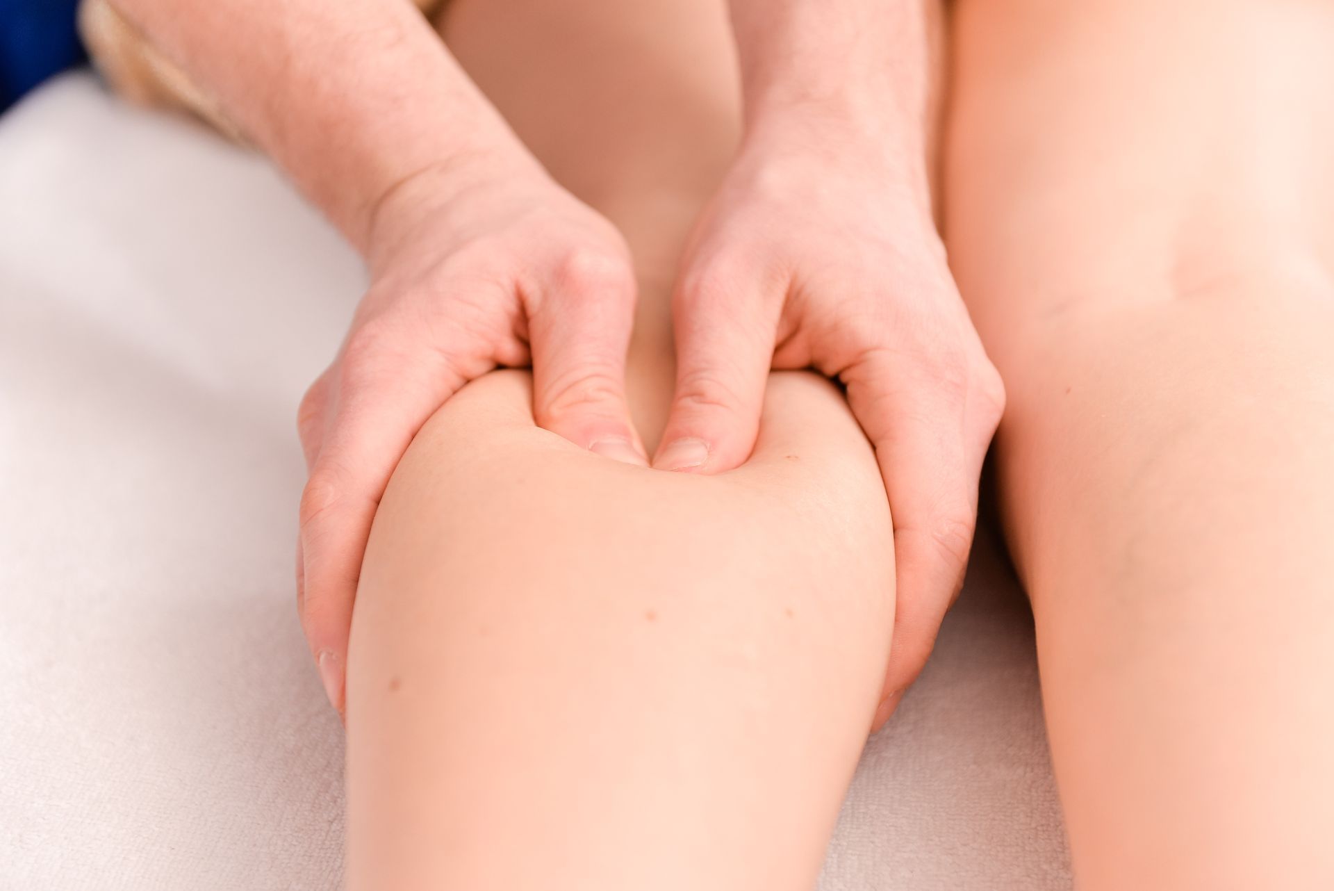 Hands massaging a light-skinned leg, focusing on the calf muscle, on a white surface.