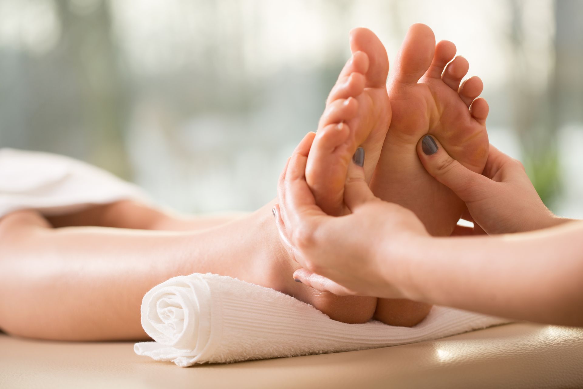 Hands massaging feet on a white towel; light skin tones, spa setting.