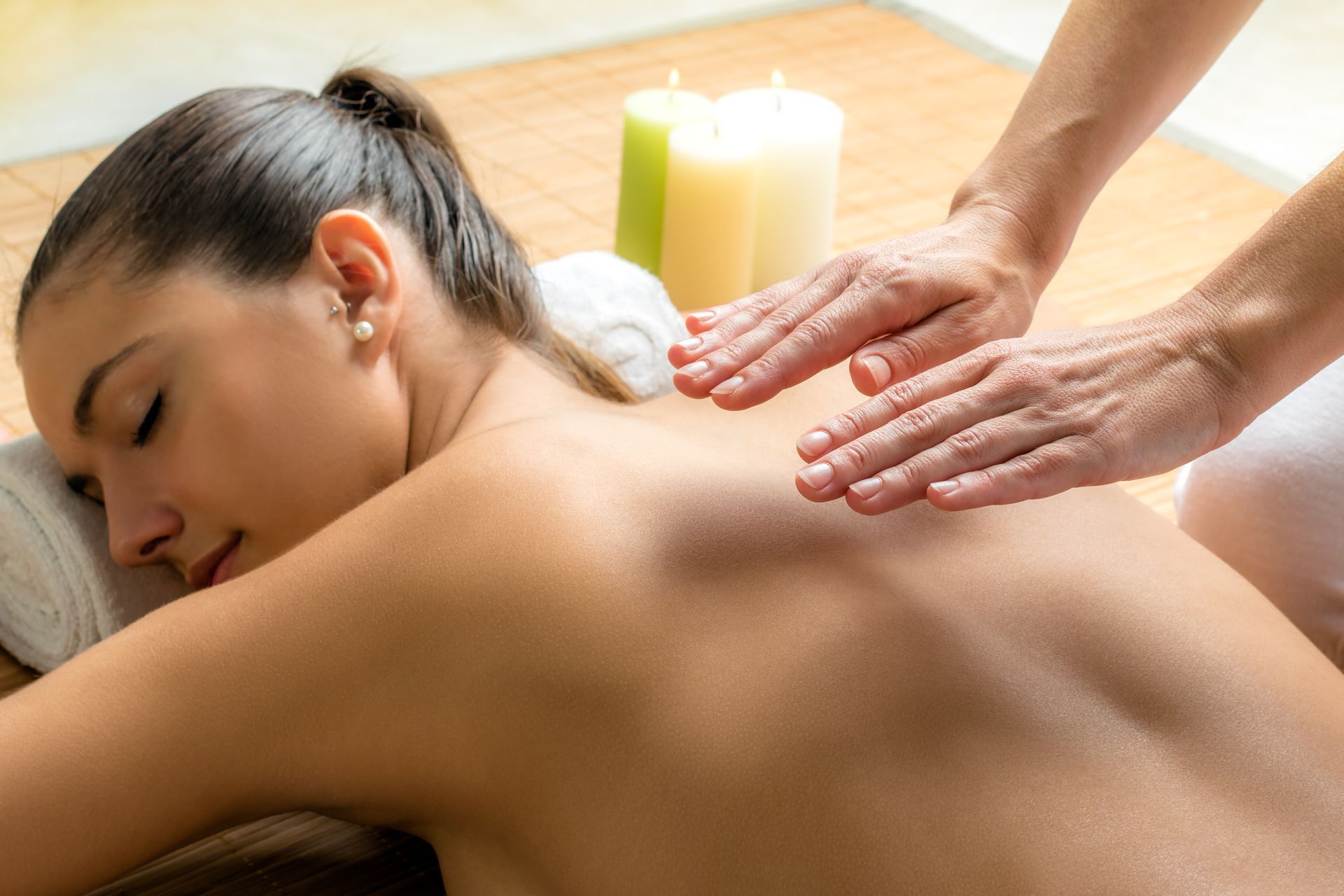 Woman receiving a back massage at a spa; hands on her back, candles in background.