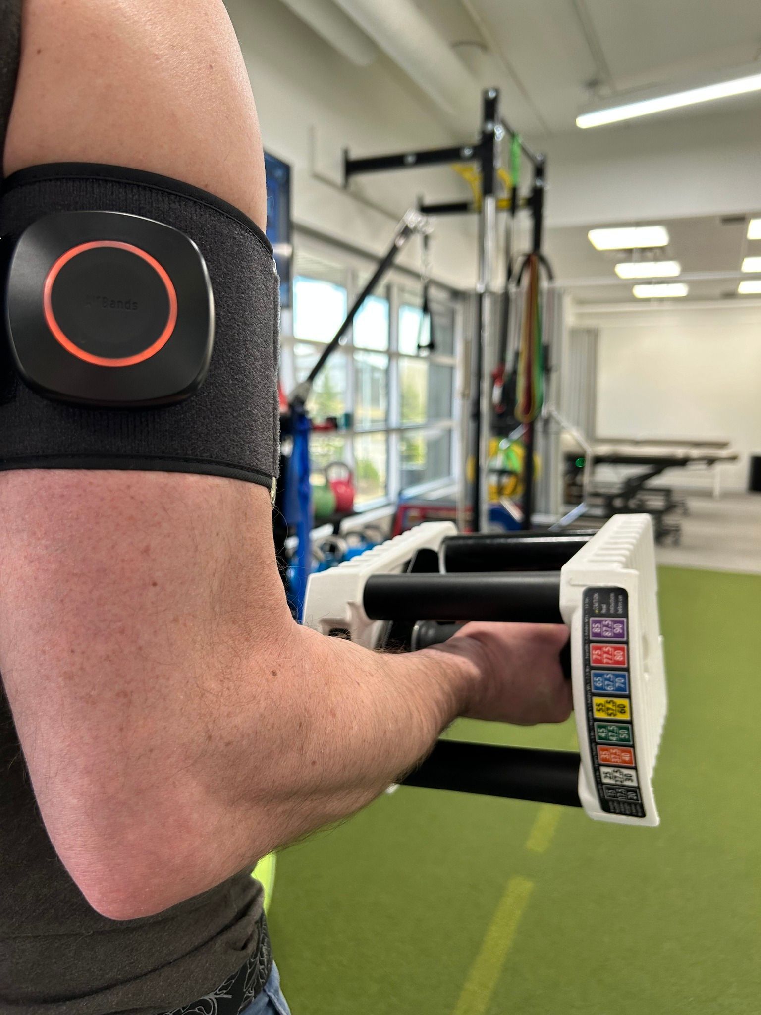 A person is holding a barbell in a gym with a device on their arm.