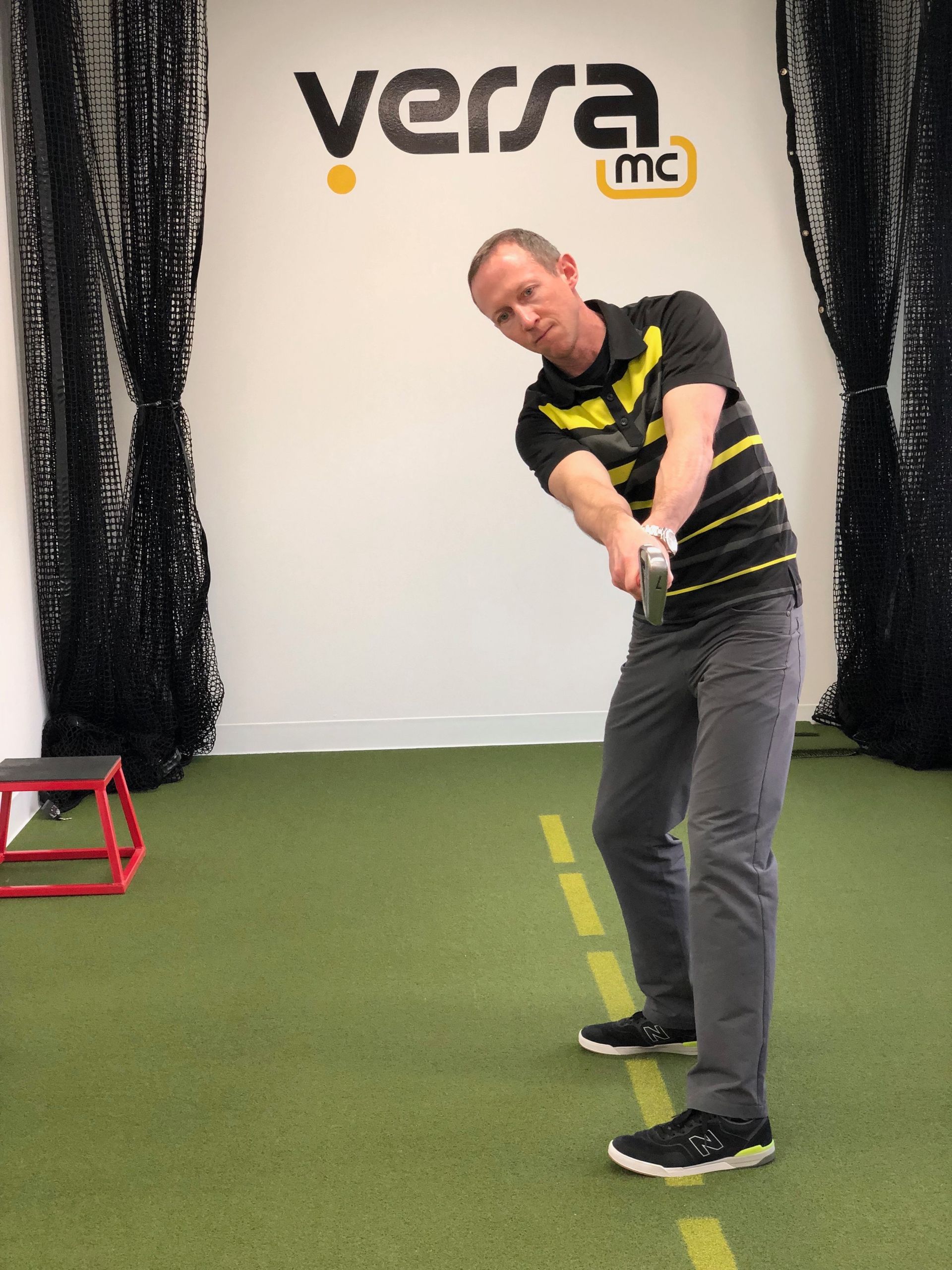 A man is swinging a golf club in front of a wall that says versa mc