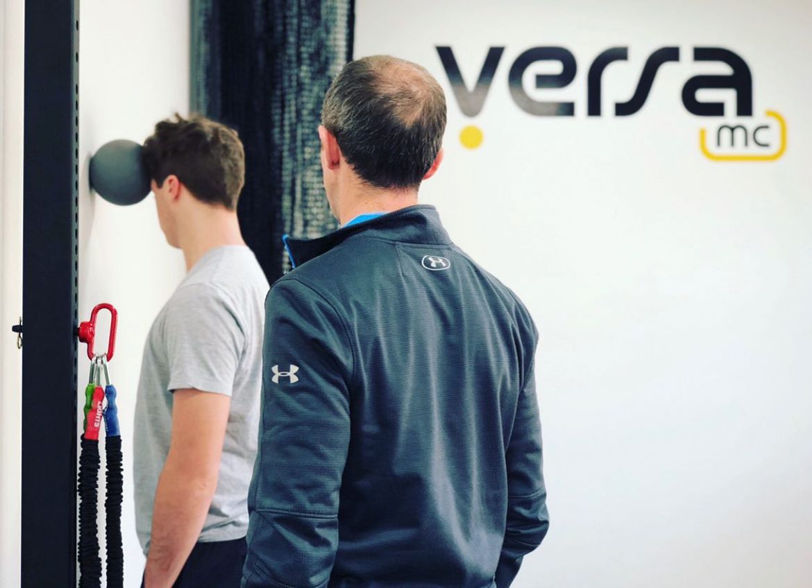 Two men are standing in front of a sign that says versa mc