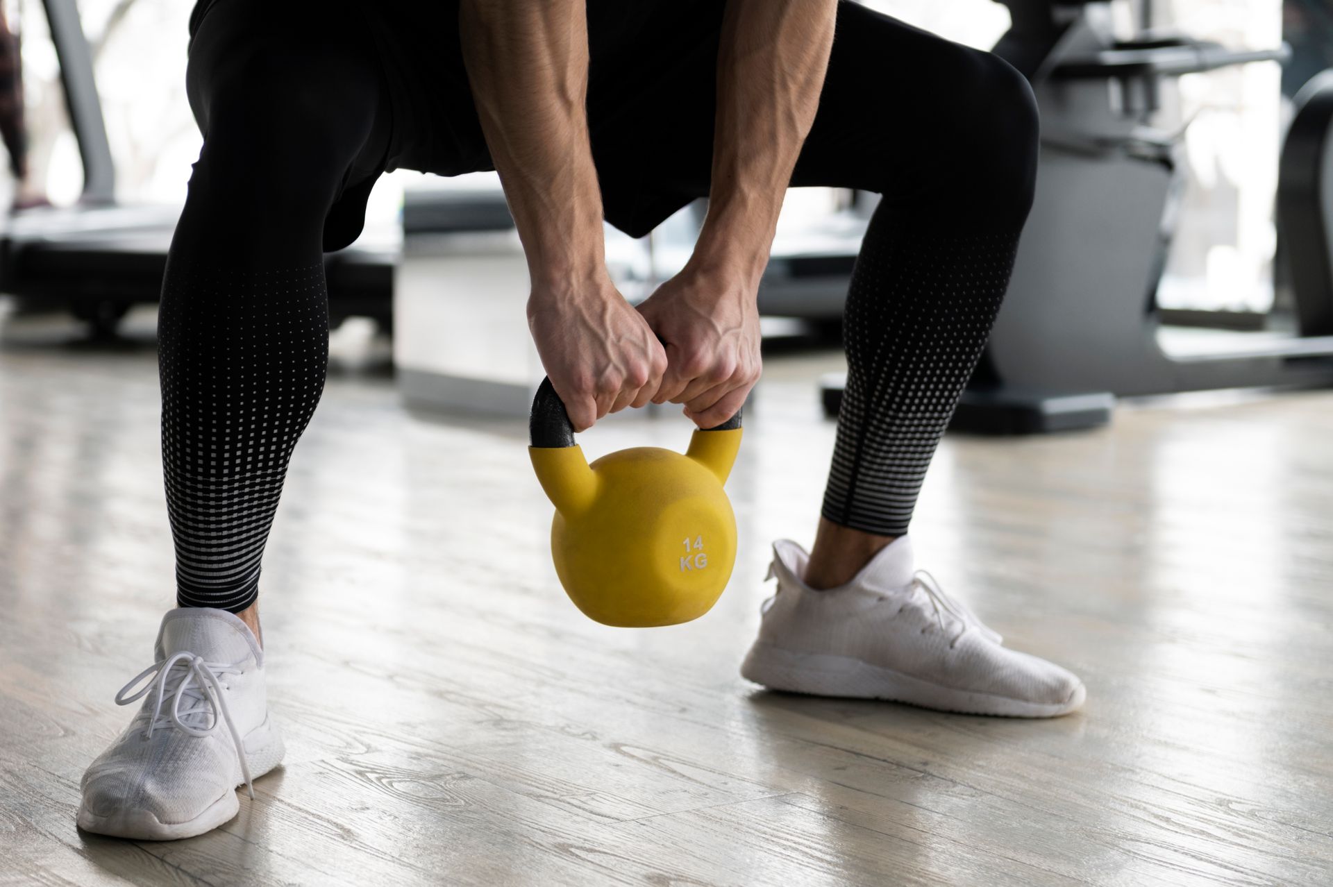 A man is squatting down while holding a yellow kettlebell in a gym.