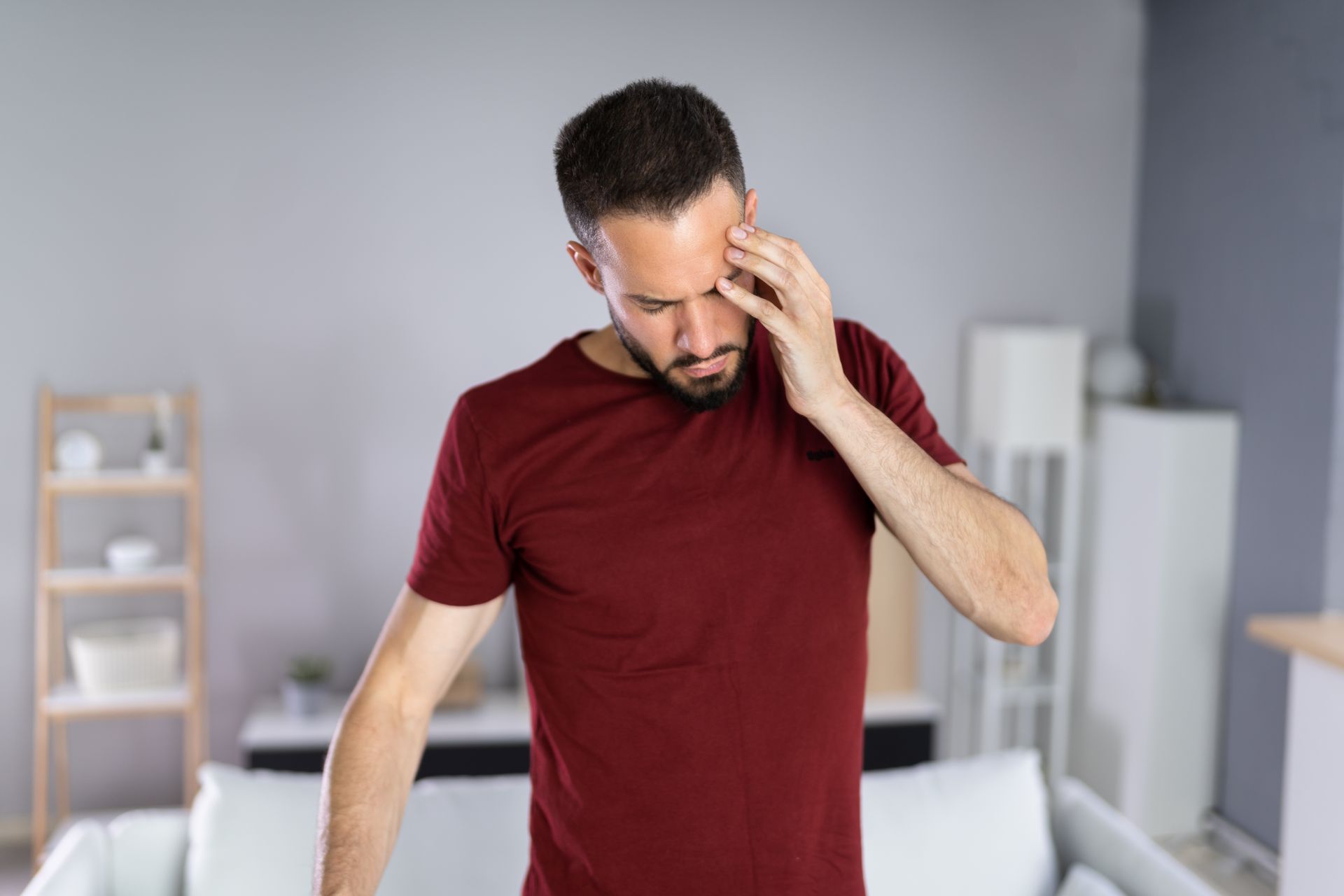 A man is standing in a living room with a headache.