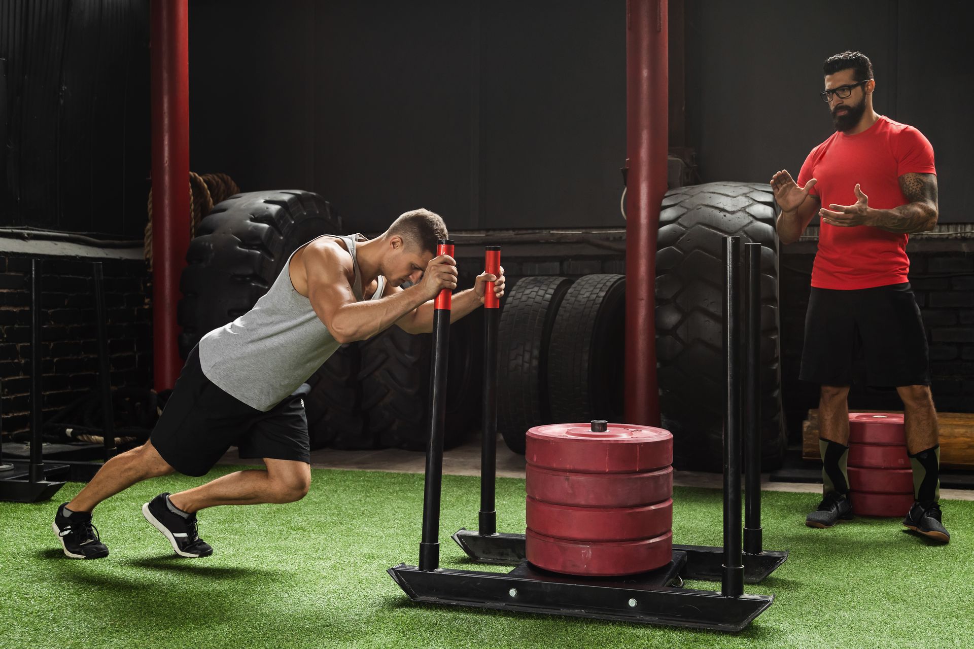 a man is pushing a sled in a gym while another man watches .