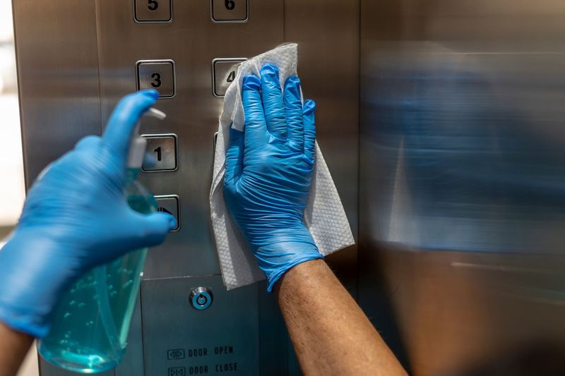 a person wearing blue gloves is cleaning the elevator buttons