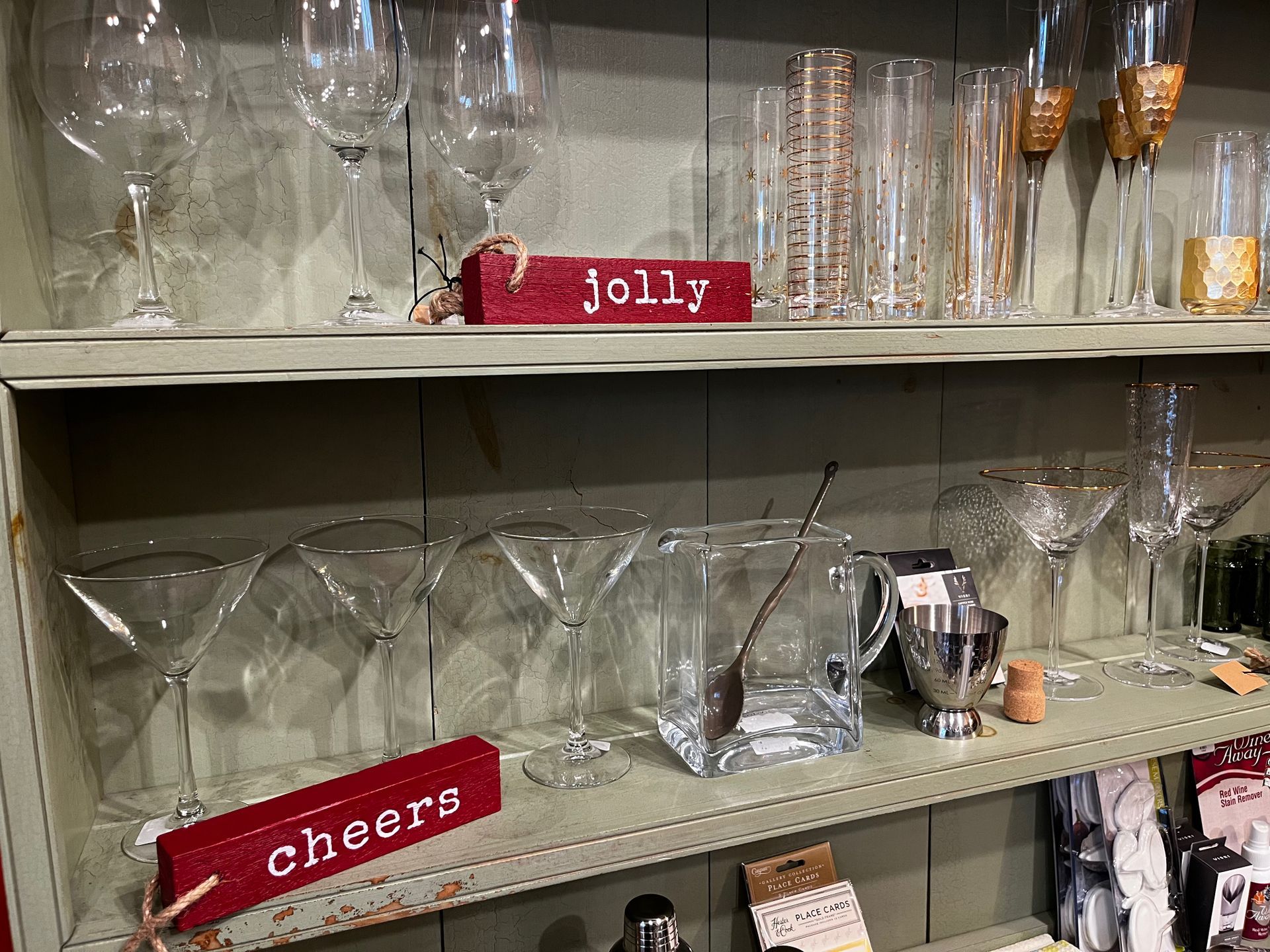 A shelf filled with wine glasses and a sign that says cheers.