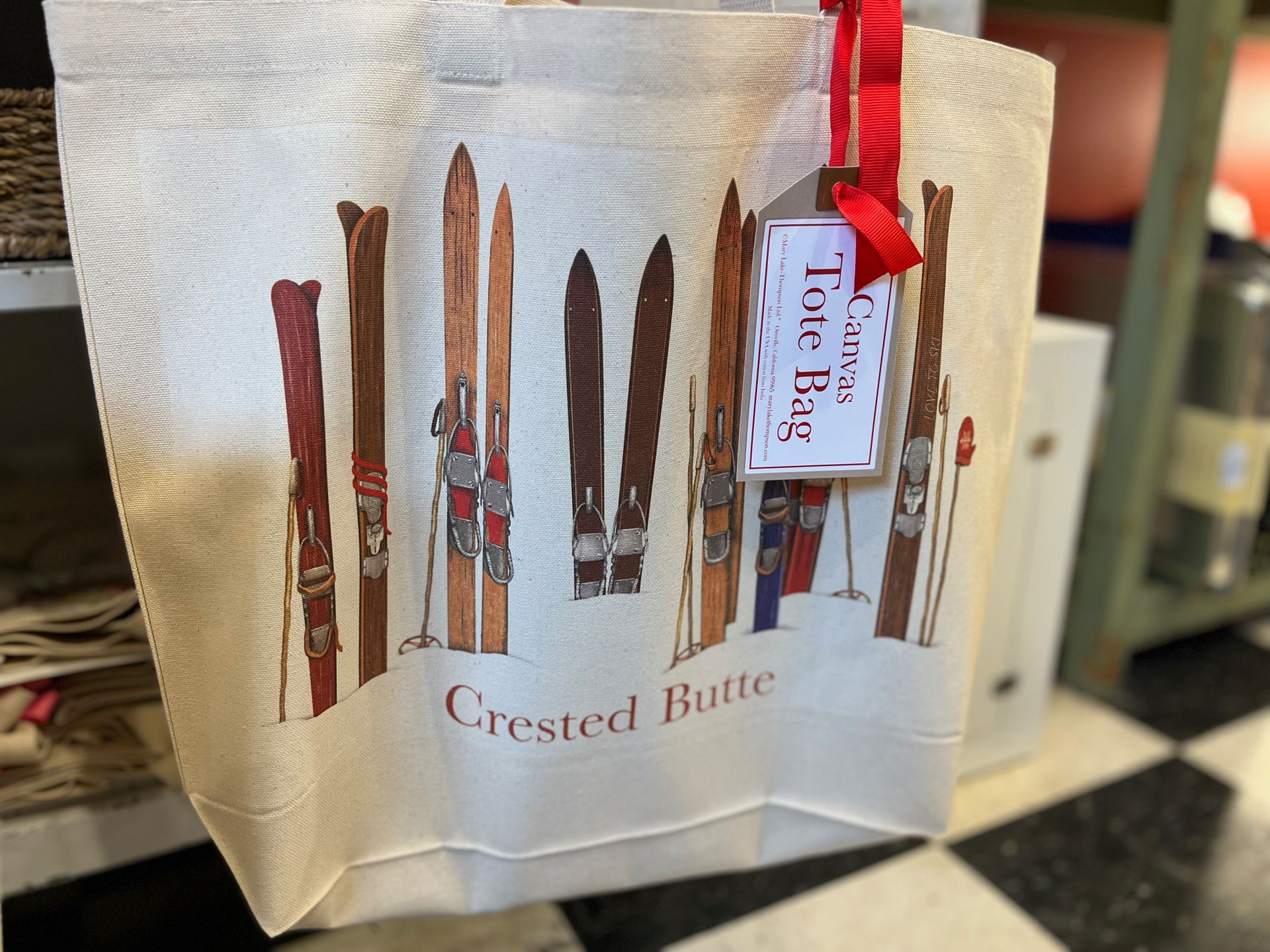 A tote bag with skis on it is sitting on a checkered floor.