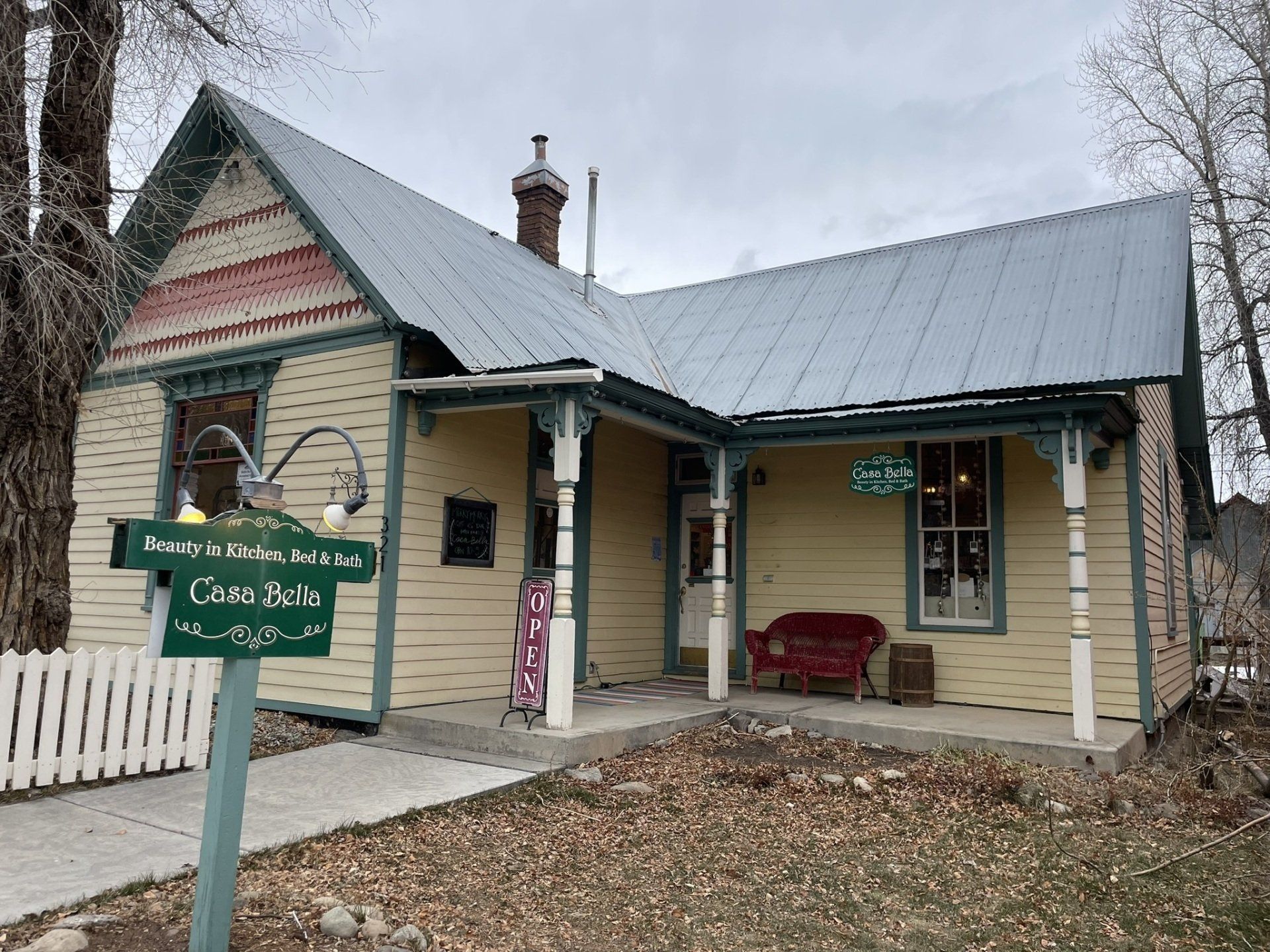 A small yellow house with a metal roof and a sign in front of it.