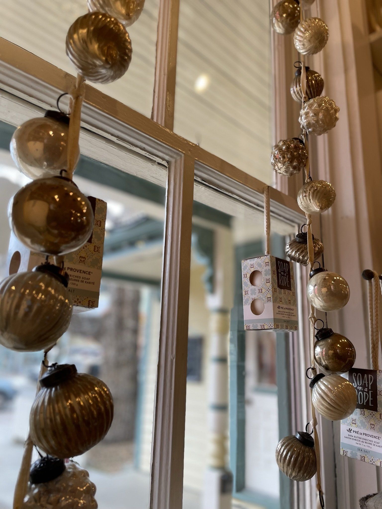 A string of gold and white christmas ornaments hanging from a window.