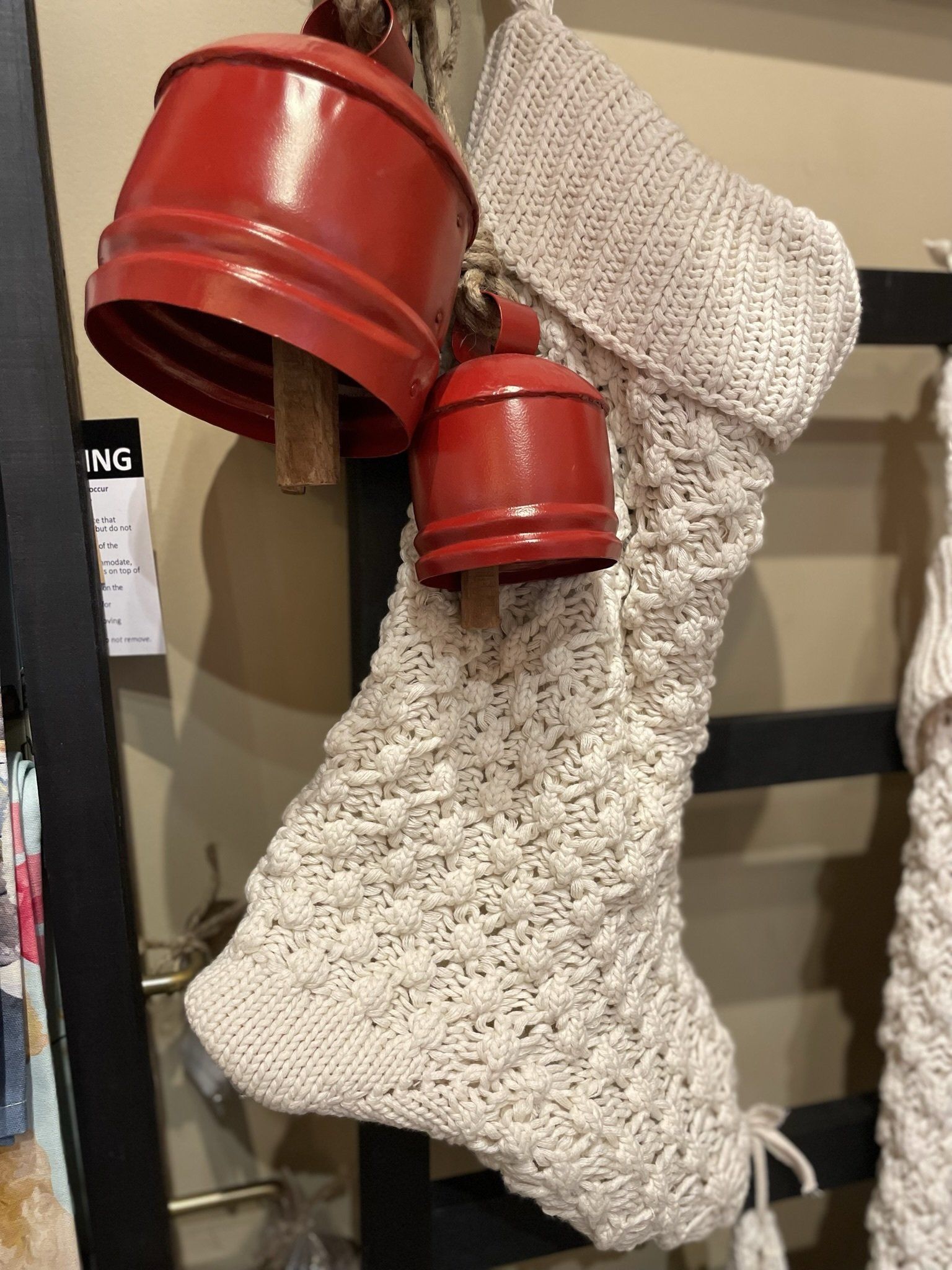A white knitted christmas stocking with red bells hanging from it.