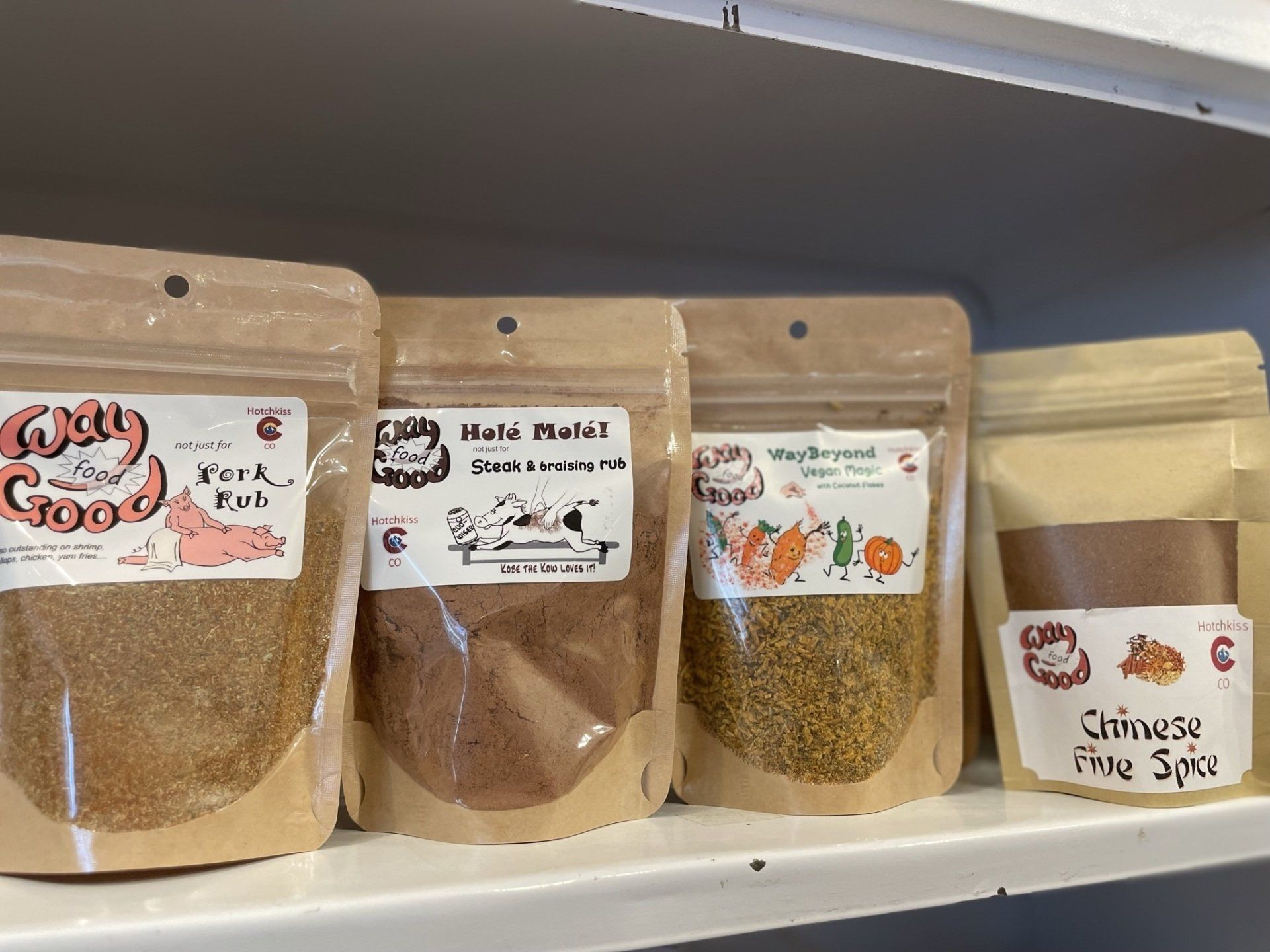 Four bags of spices are sitting on a shelf.