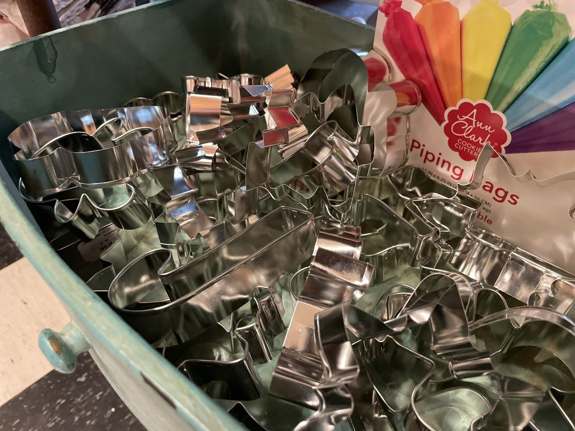 A bucket filled with stainless steel cookie cutters next to a bag of piping bags.
