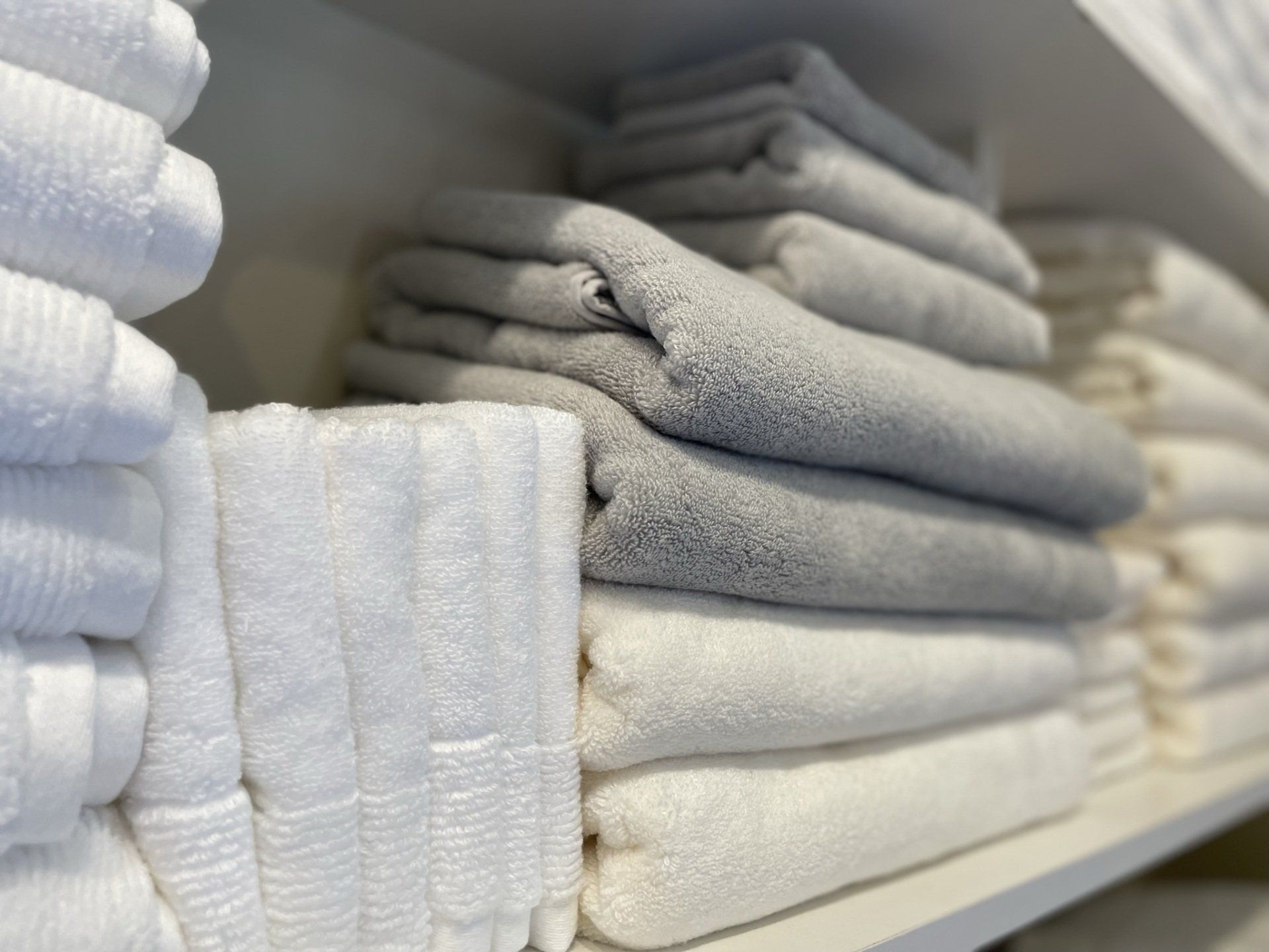 A shelf filled with stacks of white and grey towels