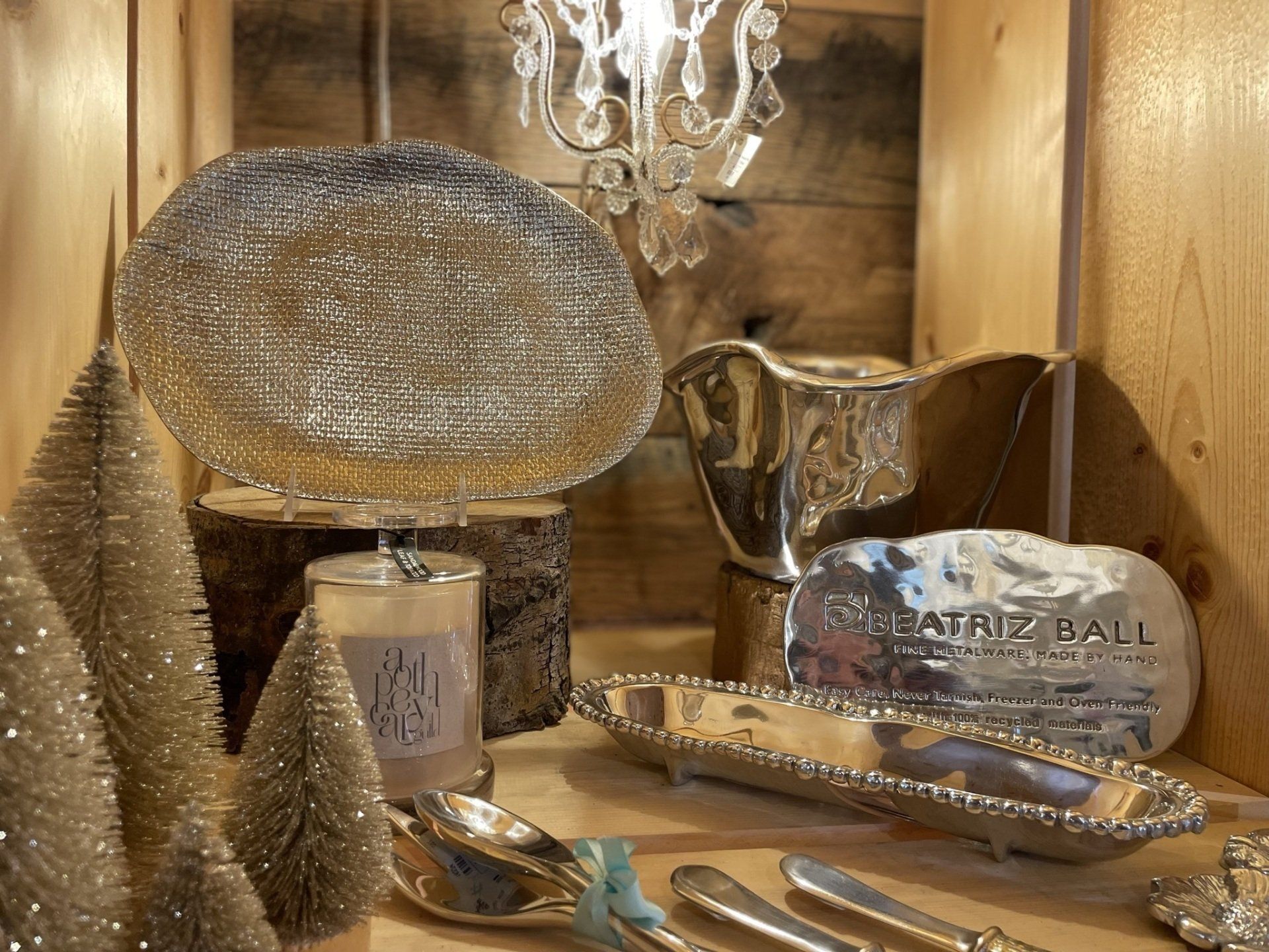 A display case filled with silver plates , silverware , candles , and christmas trees.