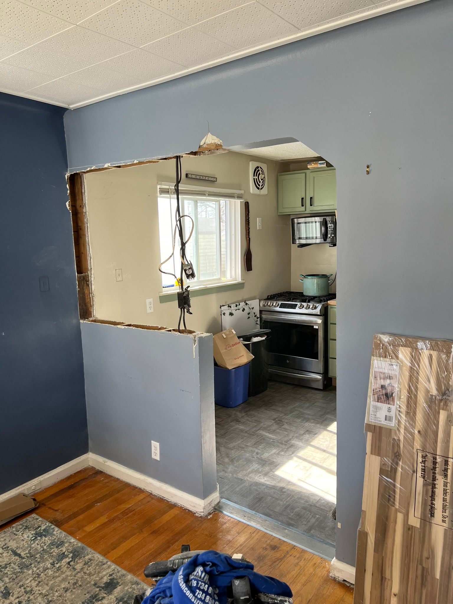 Wall opening into a kitchen with blue and grey walls, exposed wood, and appliances visible.