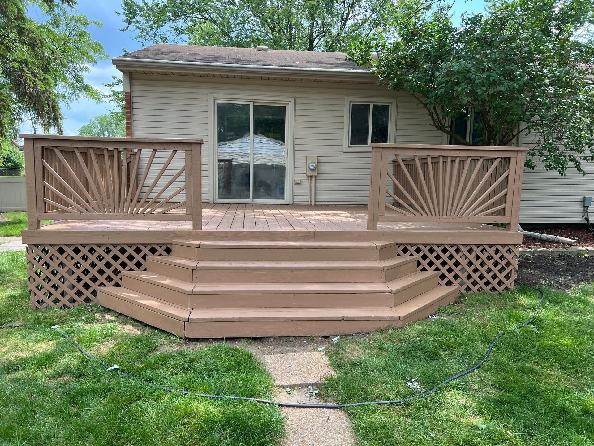 Brown wooden deck with steps, ornate railings, and a sliding glass door on a house.