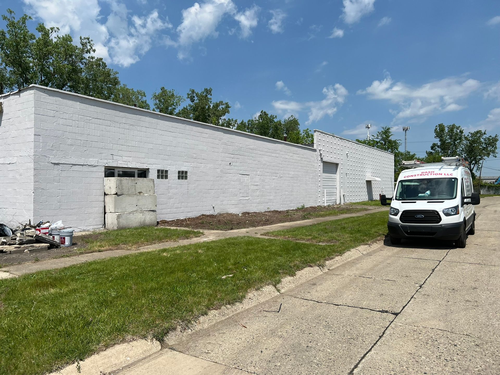 White building being painted; white van parked on street next to building; green grass and blue sky.