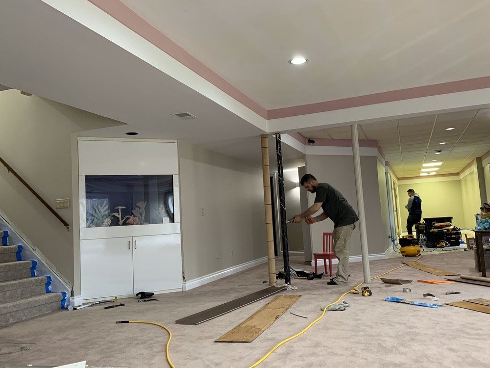 Man working on a basement renovation with tools; drywall, pink trim, staircase, aquarium.