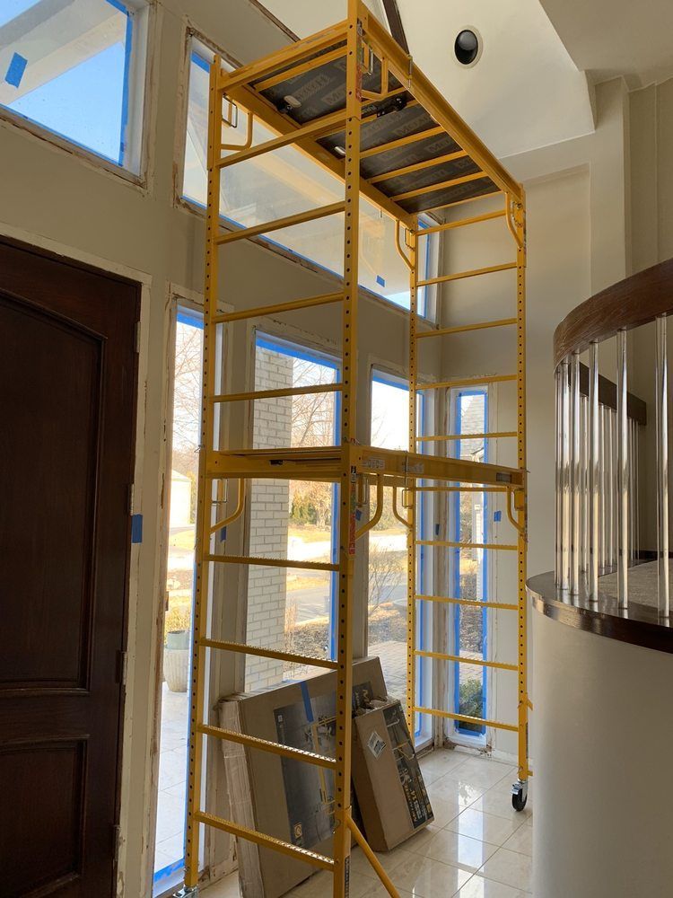 Yellow scaffolding inside a home near large windows and a wooden door.